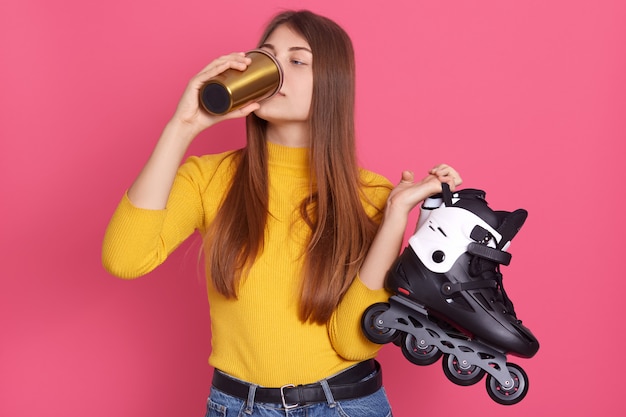 Voshititelnye Figuristki Pyushie Goryachij Kofe Ili Chaj Iz Stilnoj Termo Kruzhki Derzha V Rukah Skatyvayushiesya Konki Dama S Dlinnymi Volosami Poziruet Na Rozovoj Stene Premium Foto