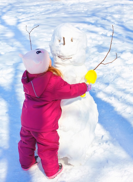 冬の公園で雪だるまを構築するかわいい女の子 雪の中で遊ぶかわいい子 プレミアム写真