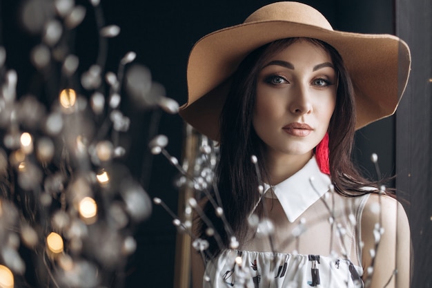 Adorable woman in beige hat and with fashion look poses in the dark studio Free Photo