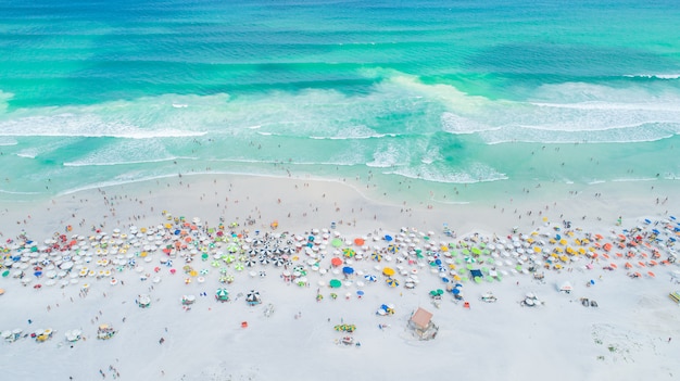Aerial locked shot of waves breaking on the shore. colourful beach umbrellas and people enjoying the