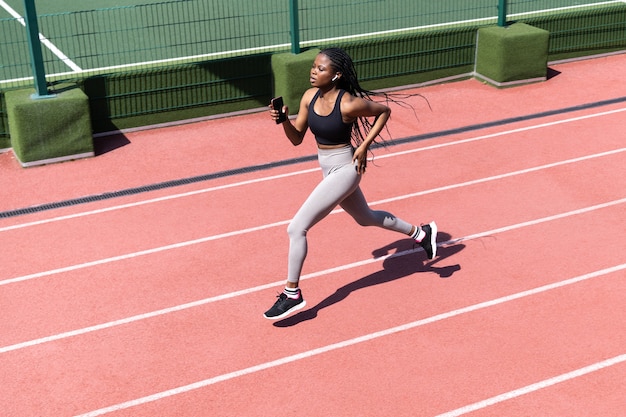 スタジアムの全力疾走で競馬場のスポーティーな黒人女性のトレーニングジョギングで走っているアフリカの女性アスリート プレミアム写真