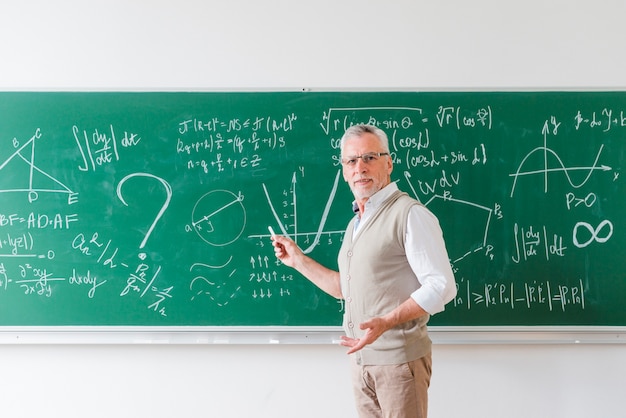 黒板にチョークで指している高齢者の数学の先生 プレミアム写真