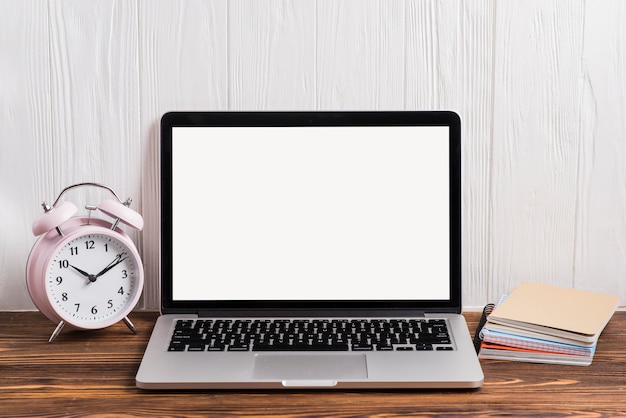 Alarm Clock An Open Laptop And Notebook Stacked On Wooden Desk