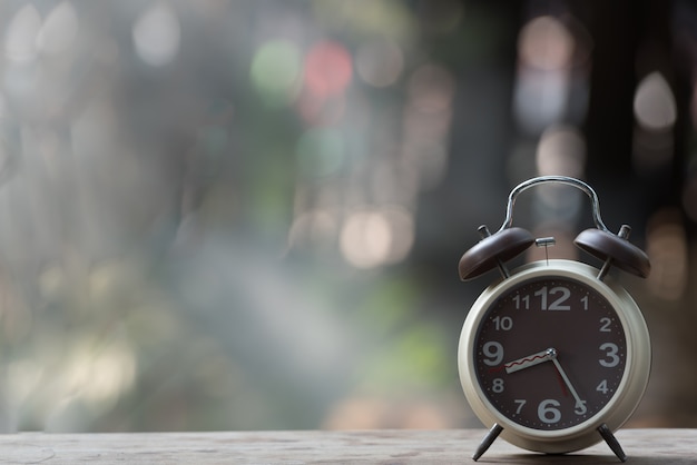 Alarm clock on wooden table with green nature bokeh background. Premium Photo