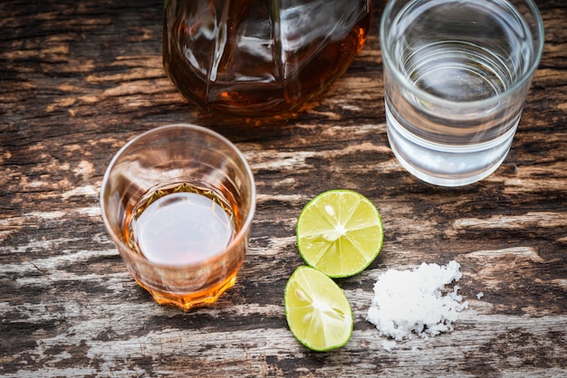 Alcoholic drinks and lemon salt on rustic wood background brandy in a glass with alcohol bottles and water, vodka rum cognac tequila and whiskey Premium Photo
