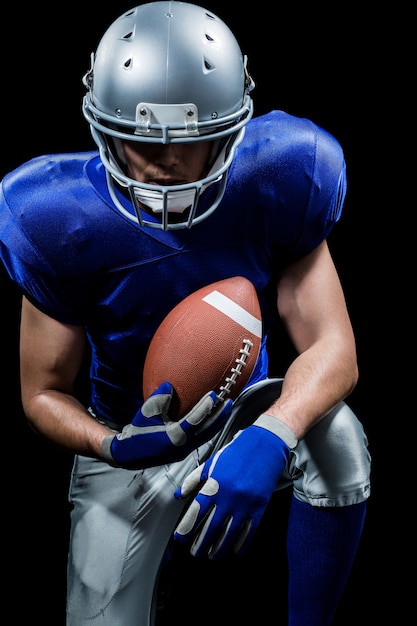 Premium Photo | American football player holding ball while kneeling