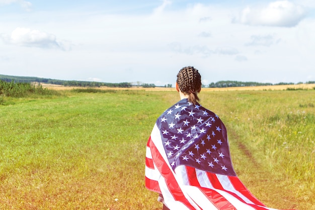 アメリカの国旗に包まれた小麦畑でアフロブレードを持ったアメリカ人の若い女性 プレミアム写真