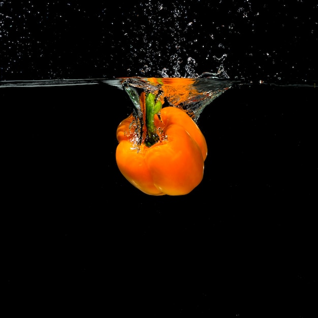 黒い背景に水に落ちるオレンジ色のピーマン 無料の写真