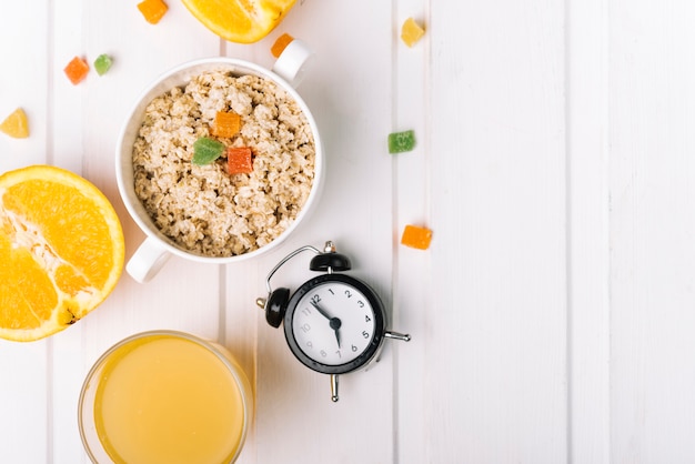 An orange glasses and oatmeal porridge with alarm clock on white table Free Photo