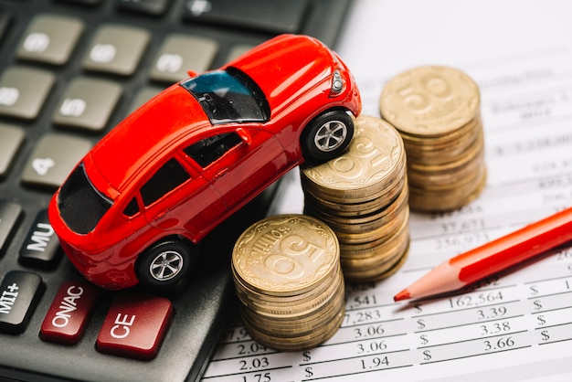 An overhead view of toy car over calculator and coin stack on financial report Free Photo