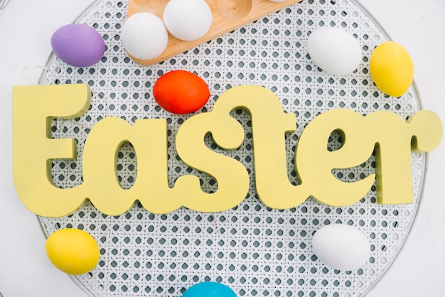 白い丸いテーブルの上のカラフルな卵と黄色のイースター単語の俯瞰 無料の写真