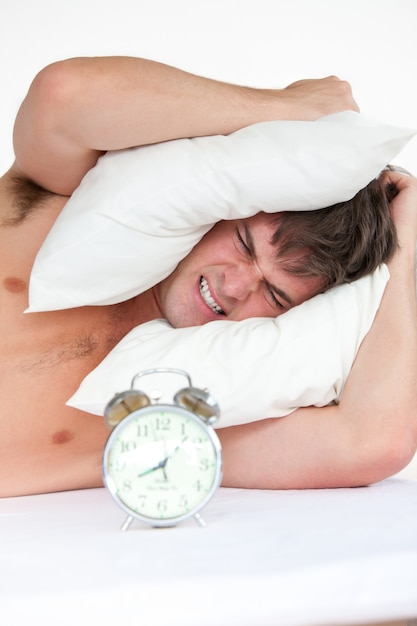 Premium Photo | Angry man woken up by his alarm clock putting pillow on ...