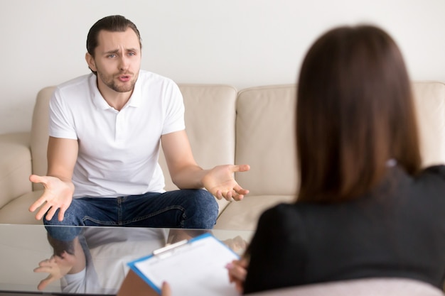 Angry troubled man complaining to female psychotherapist, talking about problems Free Photo