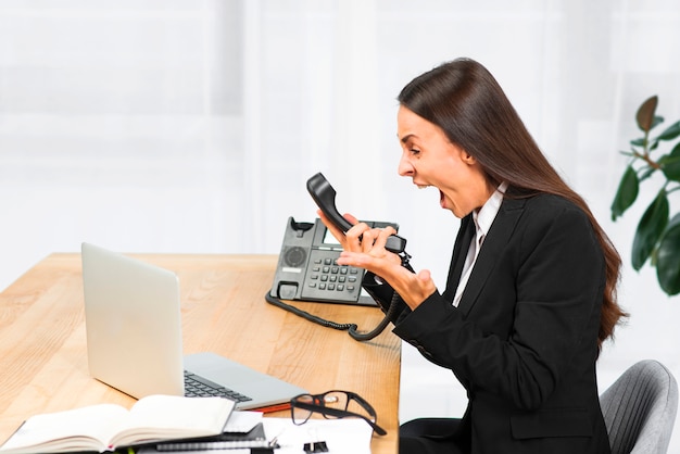 An angry young businesswoman sitting on chair shouting on telephone Free Photo