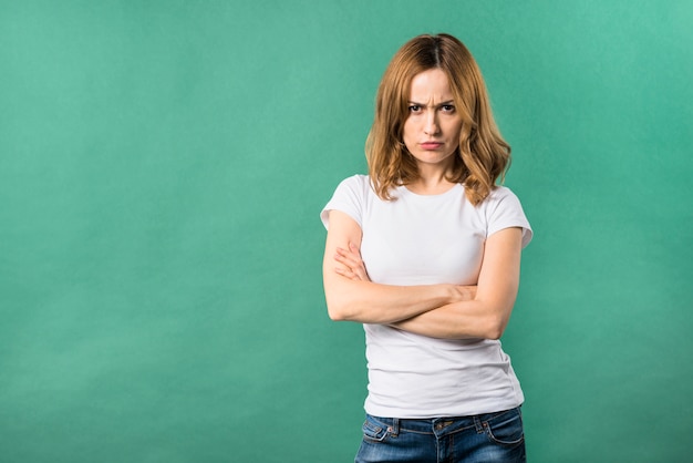 An angry young woman with arms crossed against green backdrop Free Photo