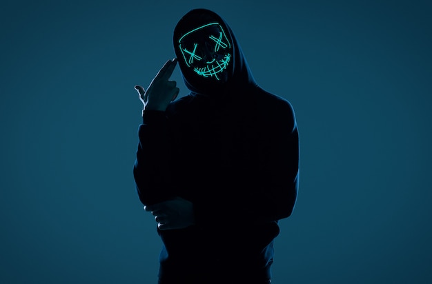 ネオンマスクの後ろに顔を隠して黒いパーカーの匿名男 プレミアム写真