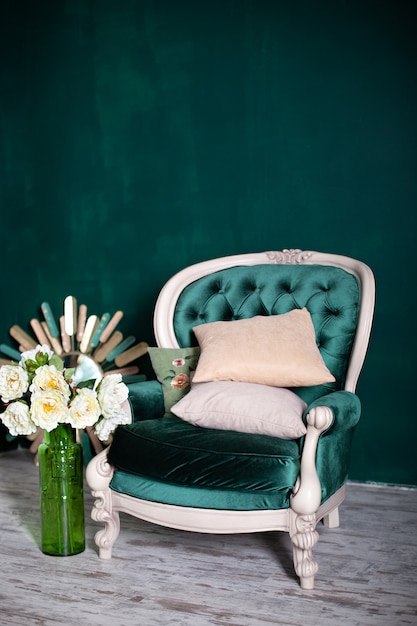 花瓶とエメラルドの壁の近くの花の花束のアンティークベルベットグリーン のアームチェア 緑の背景に分離されたアームチェア リビングルームのヴィンテージの椅子 家の家具 クラシックインテリアグリーンソファ プレミアム写真