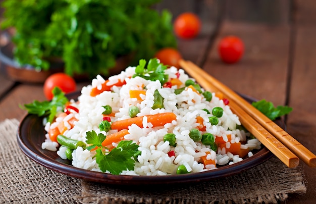 Appetizing healthy rice with vegetables in white plate on a wooden table. Free Photo