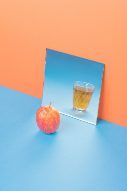 Free Photo | Apple near glass with juice in mirror on blue table isolated