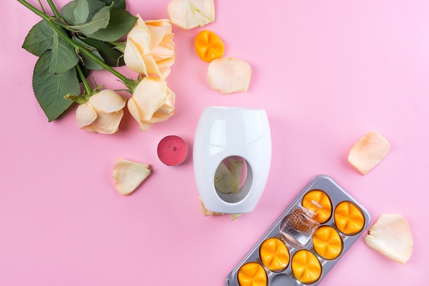 Aroma lamp with essential wax and yellow roses on pink background Premium Photo