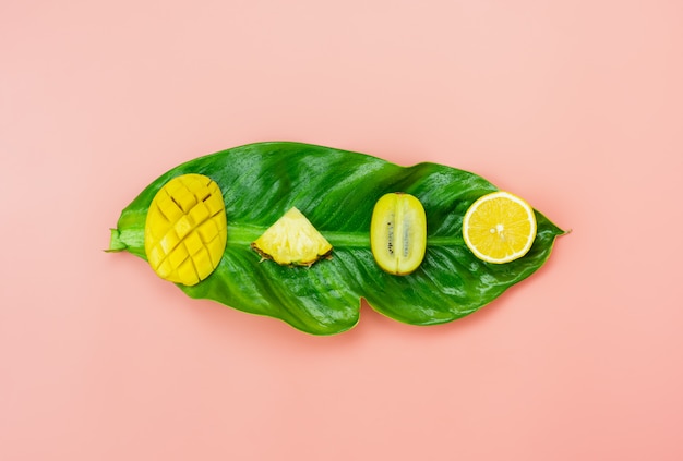 Arrangement sliced various kiwi mango lemon and pineapple on green leaves items on pink paper Premium Photo