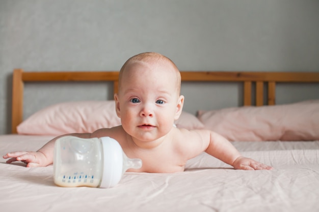 Artificial feeding. the baby lies on the bed on her tummy and looks at the feeding bottle in front of him with the adapted milk formula Premium Photo