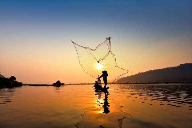 Asia fisherman net using on wooden boat casting net sunset or sunrise in the mekong river Premium Photo