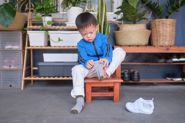 Premium Photo Asian 3 Years Old Toddler Kindergarten Kid Sitting Near Shoe Rack Near Front Door Of His House And Concentrate On Putting On His Own Socks