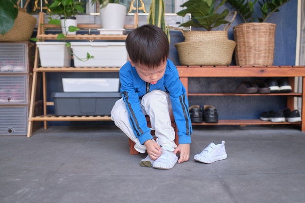 Premium Photo Asian 3 Years Old Toddler Kindergarten Kid Sitting Near Shoe Rack Near Front Door Of His House And Concentrate On Putting On His White Shoes Sneakers