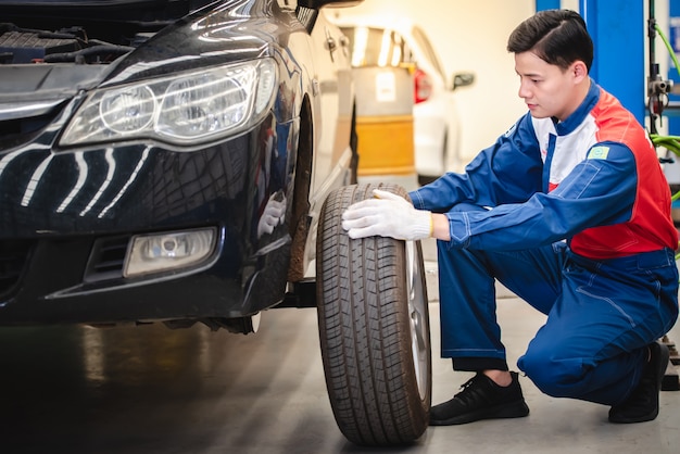 A mechanic is removing the wheel and inspecting the tire and wheel structure while rotating the tires as a part of a spring car care routine.