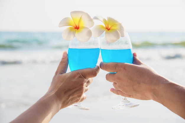 波の海のビーチとプルメリアの花とカクテルグラスの装飾を保持しているアジアのカップル 海の自然の概念で幸せなリラックスお祝い休暇 無料の写真