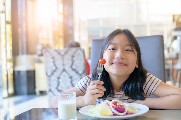 Cô bé dễ thương châu Á ăn cà chua tươi và salad vào buổi sáng.  khỏe mạnh và thư giãn với khái niệm kỳ nghỉ Ảnh cao cấp