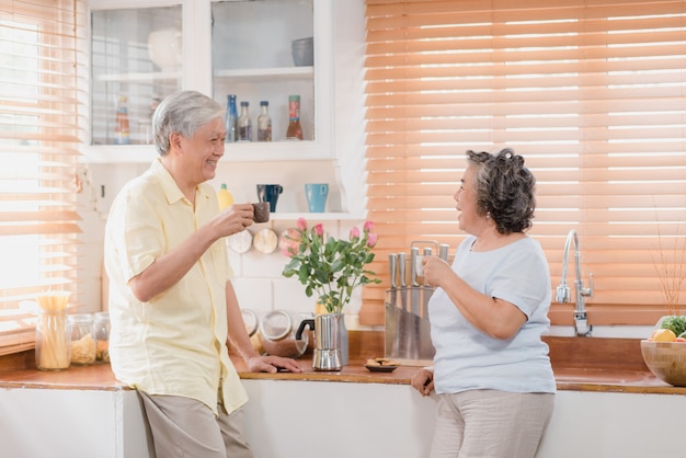 Asian elderly couple drinking warm coffee and talking together in kitchen at home. Free Photo