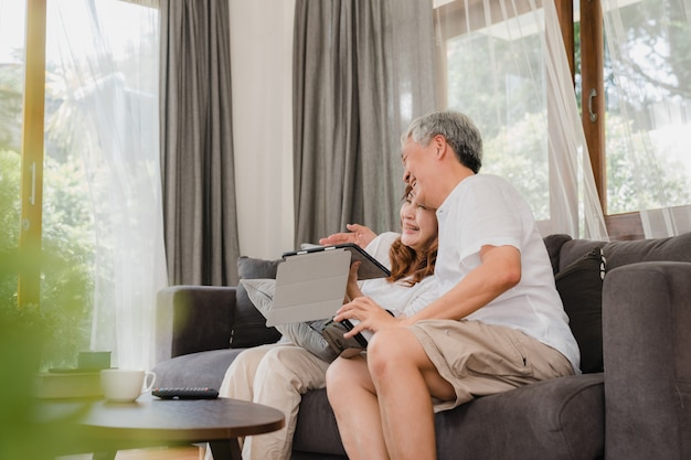 Asian elderly couple using tablet and virtual reality simulator playing games in living room, couple feeling happy using time together lying on sofa at home. lifestyle senior family at home concept. Free Photo