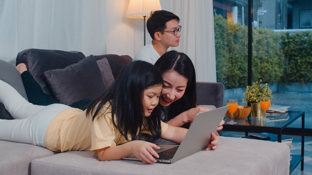 Free Photo | Asian family enjoy their free time relax together at home.  lifestyle mom and daughter using laptop watch movie on internet, dad watch  tv in living room in modern home .