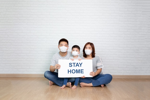 Premium Photo | Asian family wearing protective medical mask for prevent  virus covid-19 holding white paper with stay at home on hand and sitting  together on floor at home