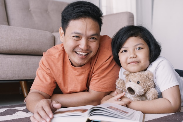 Asian Father And Daughter Are Reading Book While Lying On The Carpet In