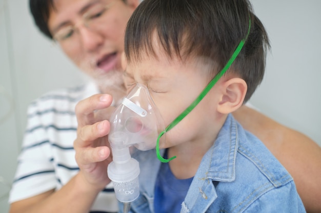Premium Photo | Asian father helping his toddler son with inhalation  therapy by the mask of inhaler. sick little kid with respiratory problem  with oxygen mask breathes through nebulizer