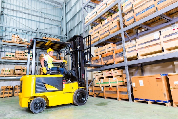Asian fork lift truck driver lifting pallet in storage Premium Photo