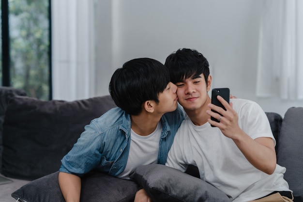 アジアのインフルエンサーゲイカップルのビデオ ブログを自宅で アジアのlgbtqの男性は リビングルームのソファに横たわっている間 ソーシャルメディアで技術携帯電話記録ライフスタイルビデオアップロードを使用して楽しいリラックスを楽しんでいます 無料の写真