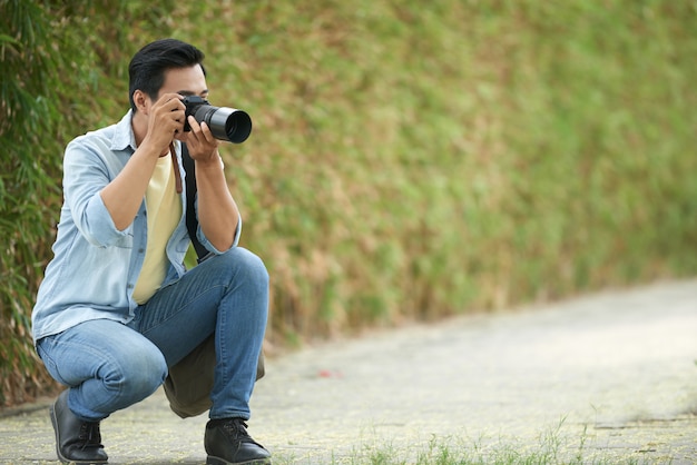 Asian man crouching down in park and taking photos with digital camera ...