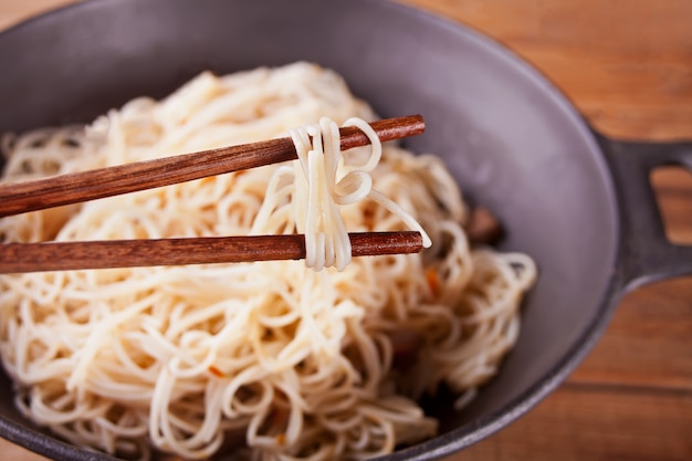 Asian noodles with beef, vegetables in wok with chopsticks, rustic wooden background. asian style dinner. chinese japanese noodles Premium Photo