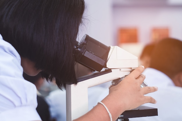Asian uniform student looking microscope in science class Premium Photo