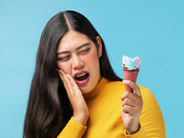 Asian woman hurt her teeth with icacream on blue background Premium Photo