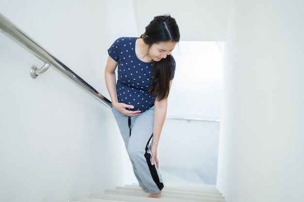 Asian woman is pregnant, she is in pain, cramps while walking up the stairs. Free Photo