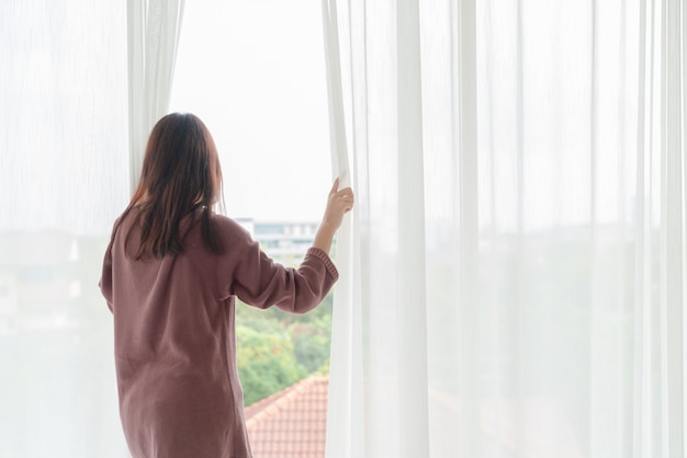 アジアの女性は朝カーテンを開ける プレミアム写真