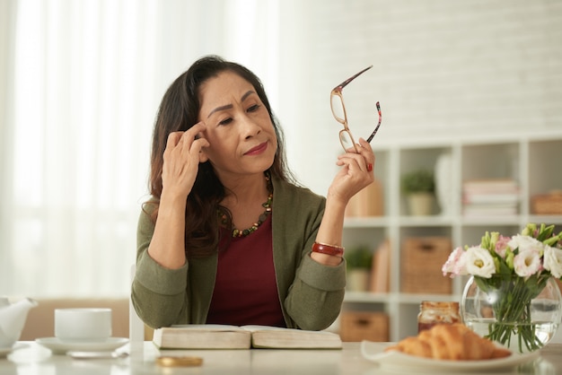 Asian woman taking off eyeglasses sitting at table in morning Free Photo