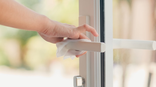 Asian woman using alcohol spray on tissue clean doorknob before open door for protect coronavirus. female clean surface for hygiene when social distancing stay at home and self quarantine time. Free Photo