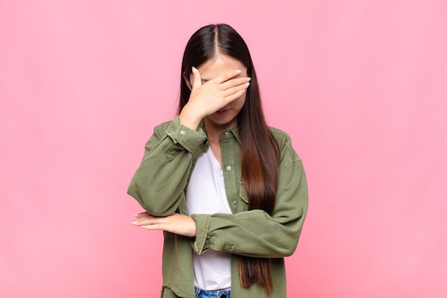 ストレス、恥ずかしがり屋、または動揺して、頭痛で、手で顔を覆っているアジアの若い女性 プレミアム写真