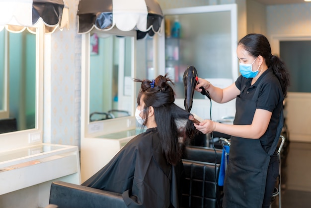 Premium Photo Asian Young Woman Wearing Face Masks To Protect Themselves From Covid 19 During Hairdresser Using Hair Dryer And Comb To Black Hair In Beauty Salon